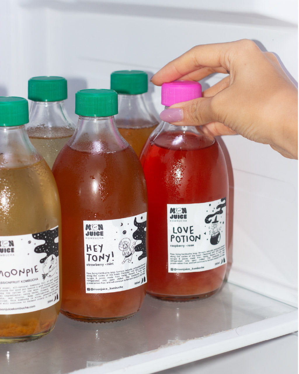 Hand selecting a bottle of kombucha from a refrigerator shelf with other bottles visible