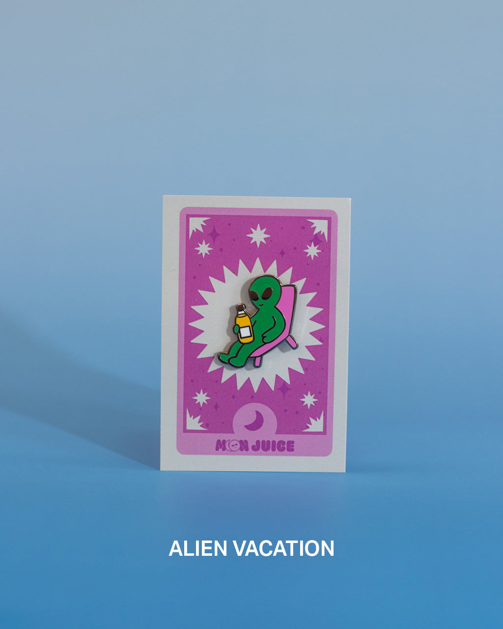 Enamel pin with a green alien reclining on a pink chair design on a pink tarot card against a blue gradient background