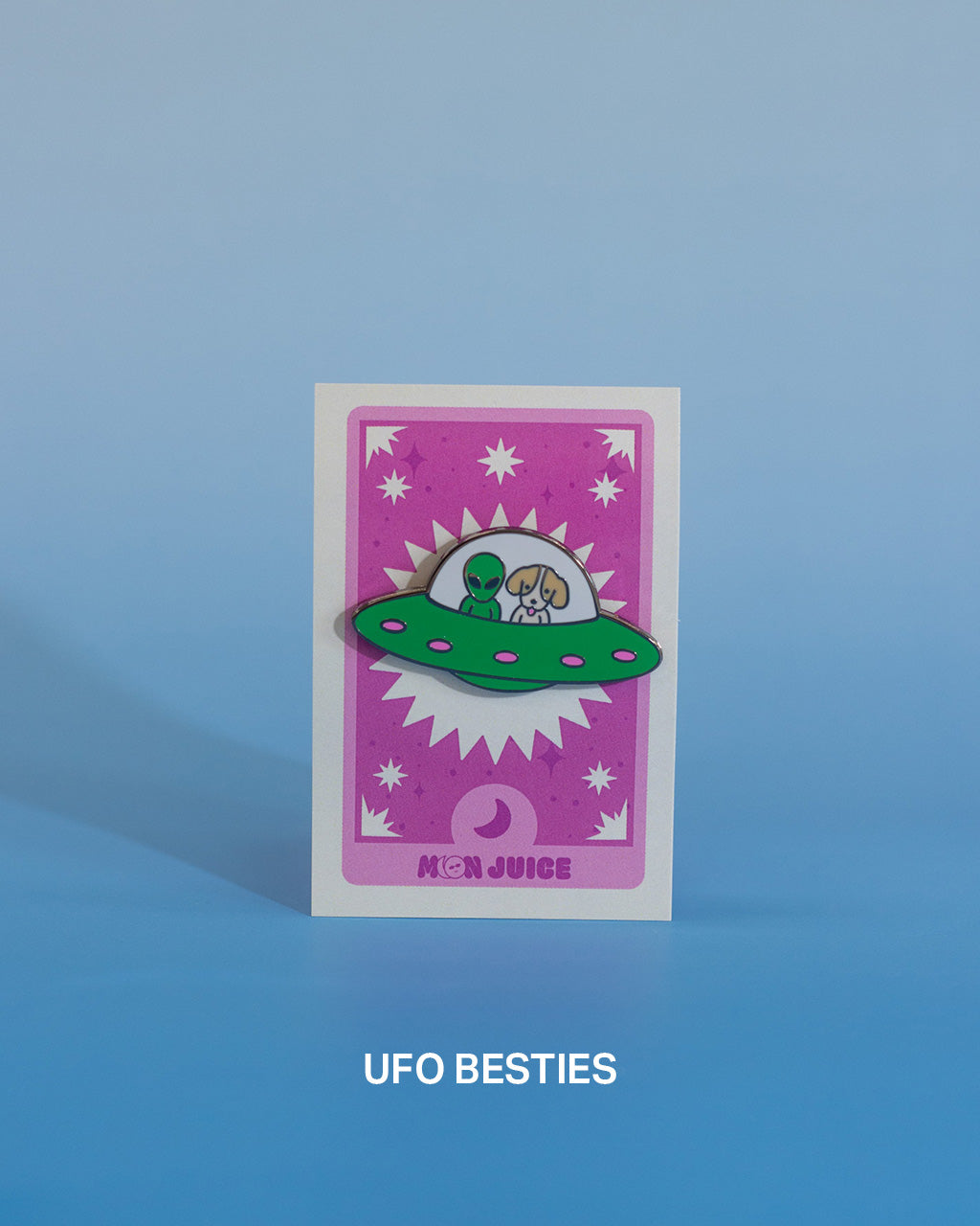 Enamel pin with a UFO design on a pink tarot card against a blue gradient background