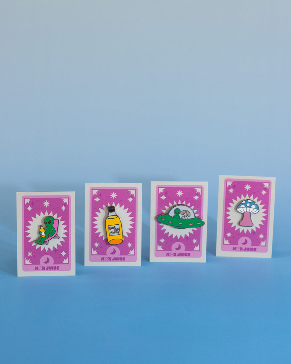 Four colorful enamel pins with various designs on pink tarot cards against a blue background