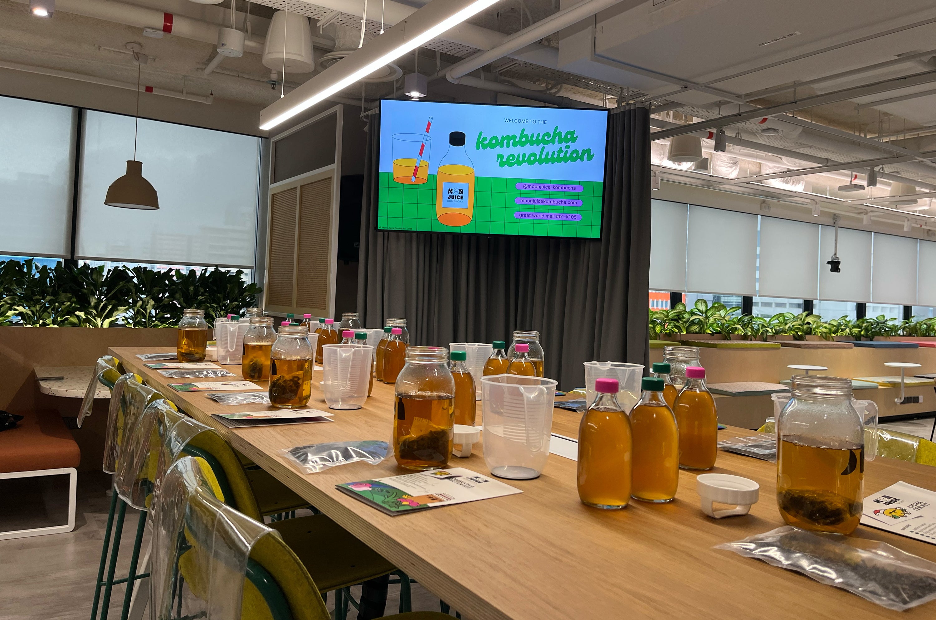 Table setup with many individual stations: each seat has a measuring jug, Moon Bottle–branded jar, 2 glass bottles of kombucha, instruction sheet, and a packet of loose leaf tea.