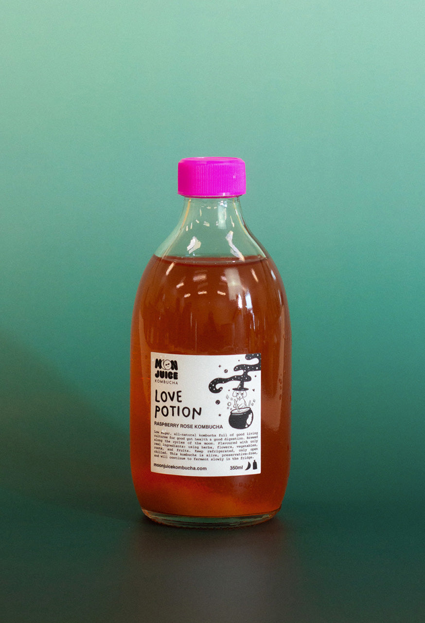 Bottle of 'Love Potion' kombucha with a pink cap on a teal gradient background