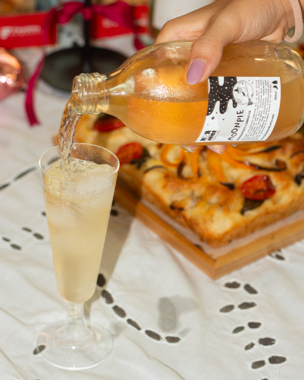 Person pouring Moonpie kombucha from a bottle into a glass with a party table setting in the background