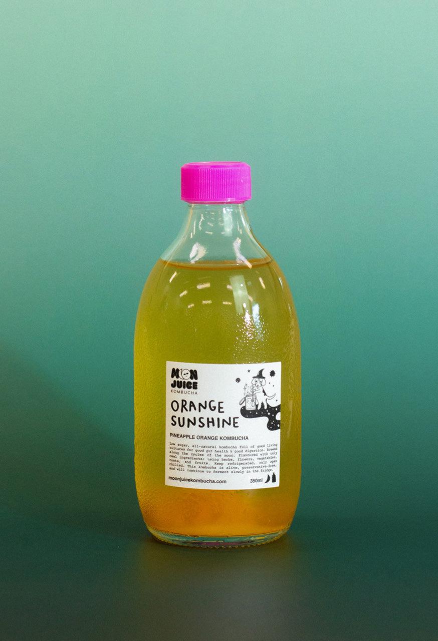 Bottle of 'Orange Sunshine' kombucha with a pink cap on a teal gradient background