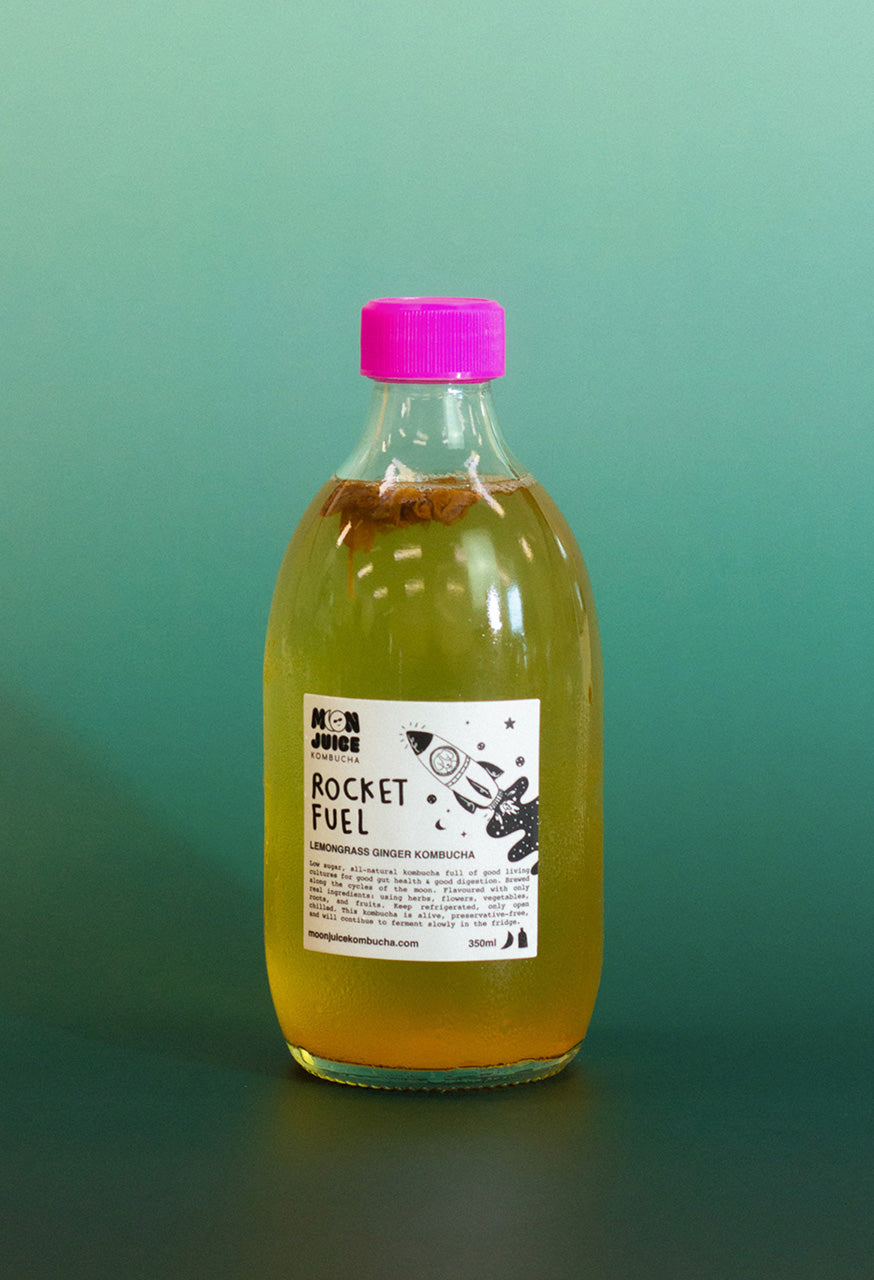 Bottle of 'Rocket Fuel' kombucha with a pink cap on a teal gradient background