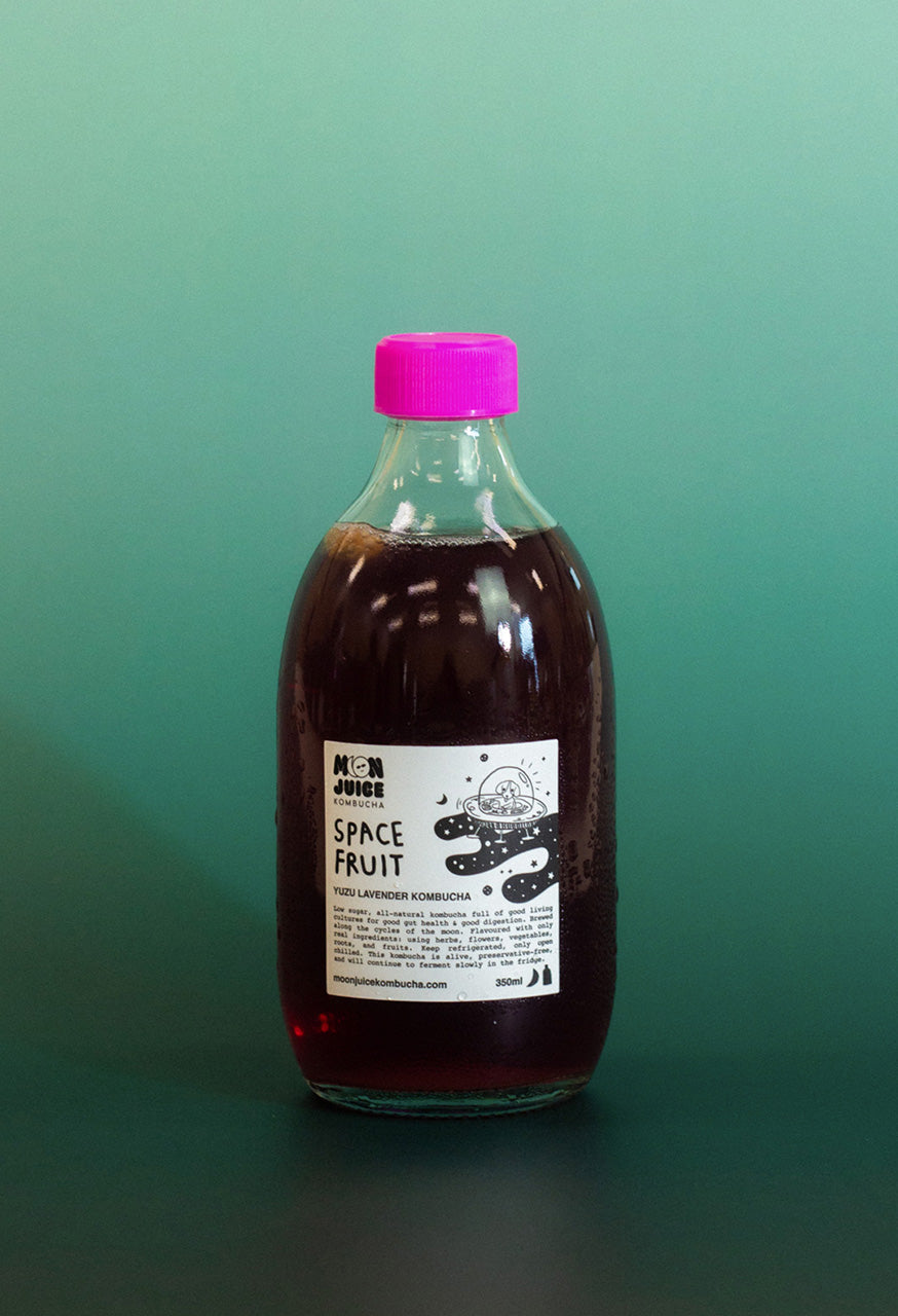 Bottle of 'Space Fruit' kombucha with a pink cap on a teal gradient background