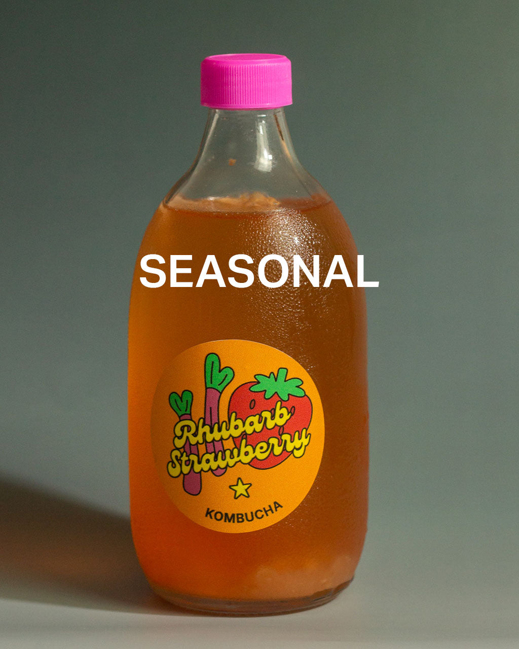 500ML Bottle of rhubarb strawberry kombucha with a pink cap on a dark teal gradient background, with the caption "SEASONAL"