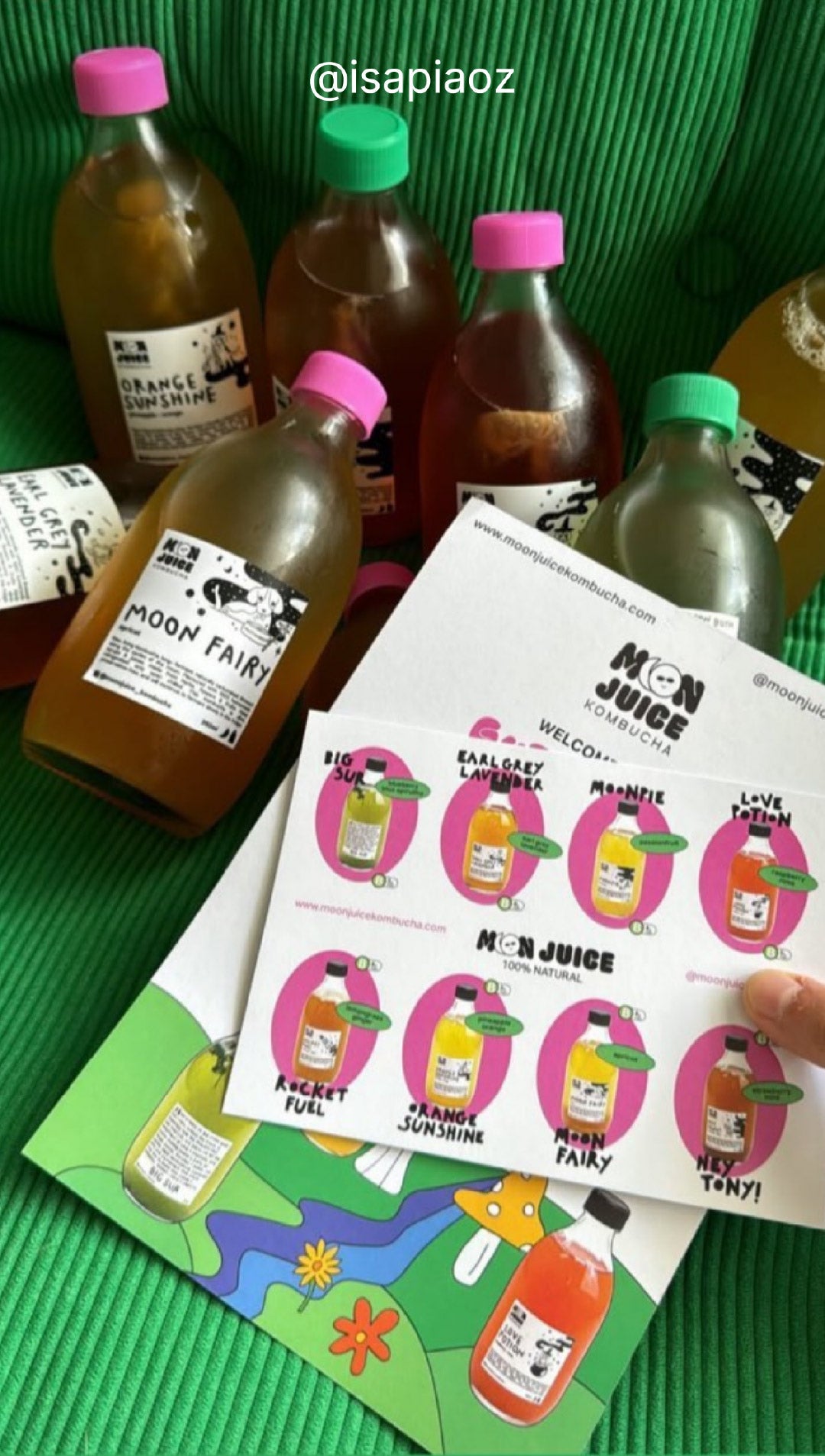 Lifestyle shot of 6 Moon Juice Kombucha bottles on a green armchair, along with a drinks catalogue. Taken by @isapiaoz