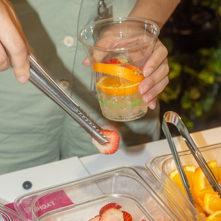 Person taking a strawberry with a tong and adding it to a cup with oranges and strawberries inside