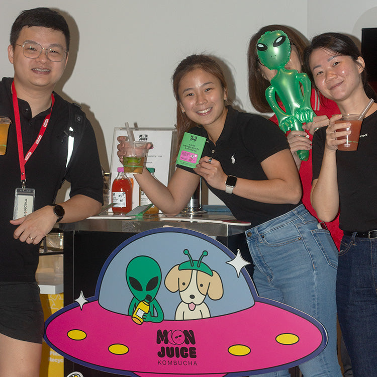 4 people holding drinks in their hands, standing in front of a kombucha cart.