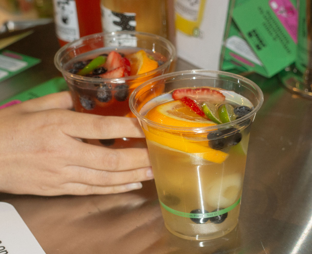Two plastic cups full of an asoortment of sliced fruits and kombucha
